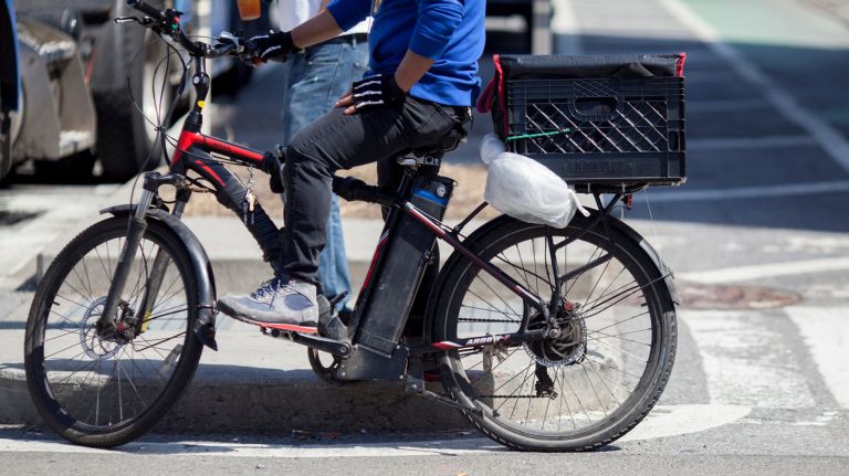 A delivery man stands on Ninth Avenue near 53th Street, with an e-bike.