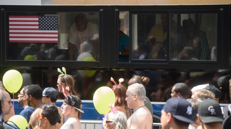 Bus riders look out of the window at people participating in the parade.