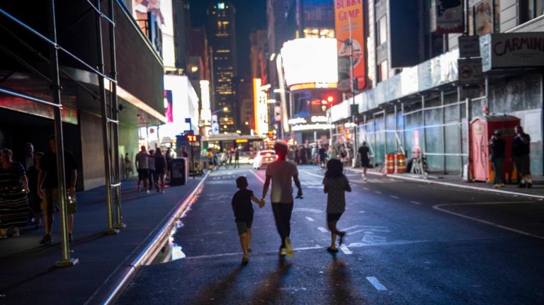 Pedestrians walking towards lights of Times Square through darkened 44th Street.