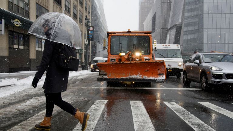A woman walks past a snow plow as she crosses Ninth Avenue in Manhattan on March 21, 2018.