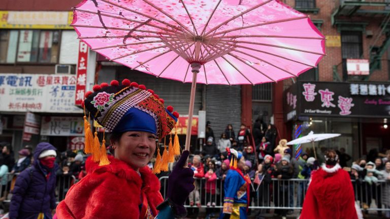 Parade-goers walk&nbsp;with pink umbrellas in their&nbsp;intricately detailed traditional dress.
