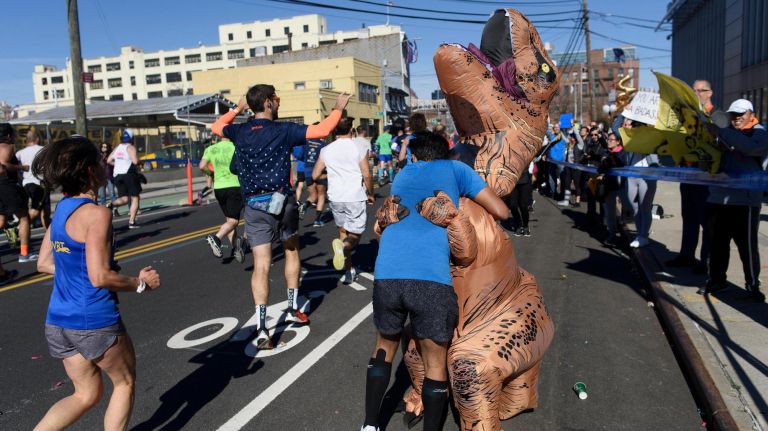 A marathon runner hugs a person dressed in a dinosaur suit in Long Island City on Sunday.