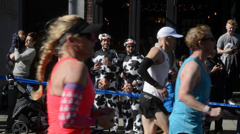 Two men in cow costumes watch as marathon runners pass in Long Island City.