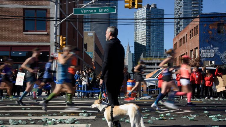 A man with a dog watches as marathon runners pass in Long Island City on Sunday.