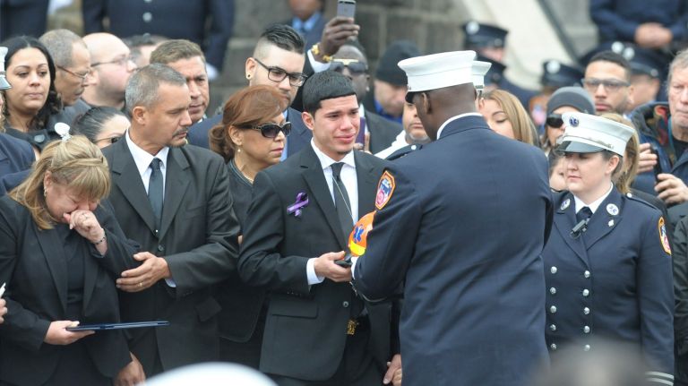 Kenneth Robles, 19, a son of FDNY EMT Yadira Arroyo, receives her helmet from FDNY Capt. Joseph Jefferson Saturday, March 25, 2017, outside of St. Nicholas of Tolentine Roman Catholic Church on University Avenue in the Bronx.
