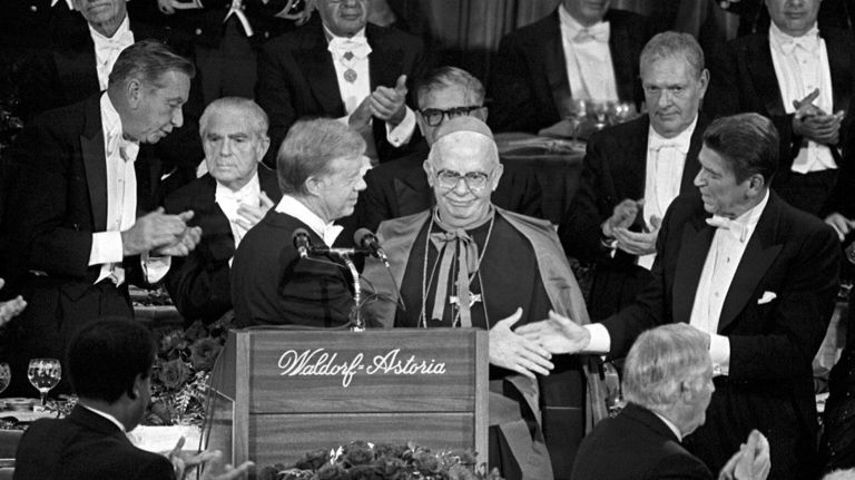 ( right,front ) President Jimmy Carter and his opponent Ronald Reagan ( left, front) extend their hands toward each other in a friendly gesture that was applauded by guests at the Al Smith Dinner. In middle is His Excellency John J. Maguire, behind are former N.Y. govenor Malcom Wilson and former NYC Mayor Abe Beame on Oct. 16, 1980 at the Waldorf Astoria Hotel in New York City.