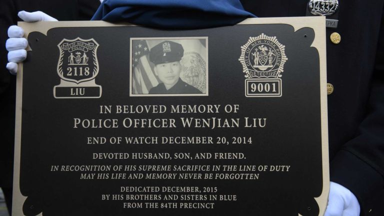 A member of the New York Police Department holds memorial plaque honoring Detective WenJian Liu at the 84th Precinct in Brooklyn on Sunday, Dec. 20, 2015. Liu and Ramos were shot and while in a squad car last December.
