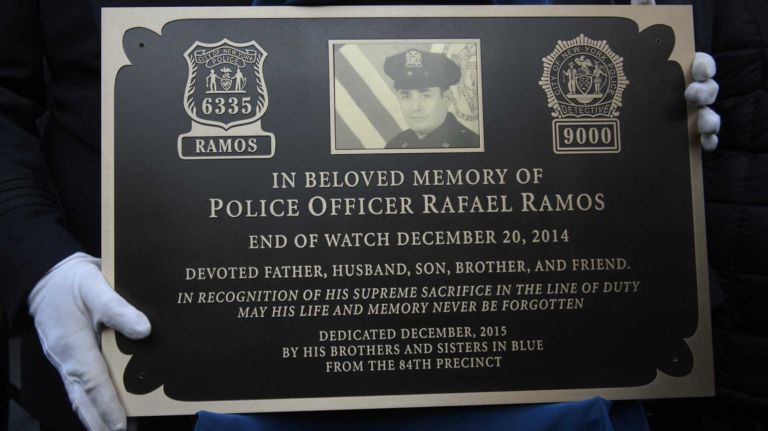 A member of the New York Police Department holds a memorial plaque honoring Detective Rafael Ramos at the 84th Precinct in Brooklyn on Sunday, Dec. 20, 2015. Liu and Ramos were shot and while in a squad car last December.