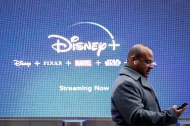 FILE PHOTO: A man looks at his phone as he passes by a screen advertising Walt Disney’s streaming service Disney+ in New York