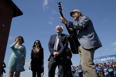 FILE PHOTO: U.S. Democratic presidential candidate and U.S. Senator Bernie Sanders listens as Guy Forsyth performs “This Land Is Your Land” at 2016 campaign rally in Austin