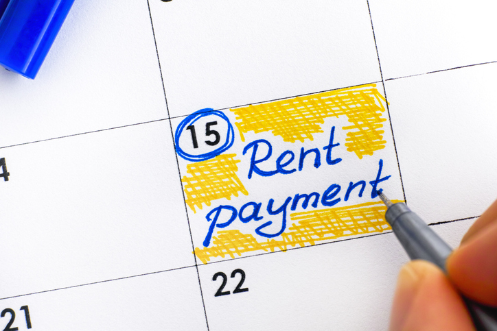 Woman fingers with pen writing reminder Rent Payment in calendar.