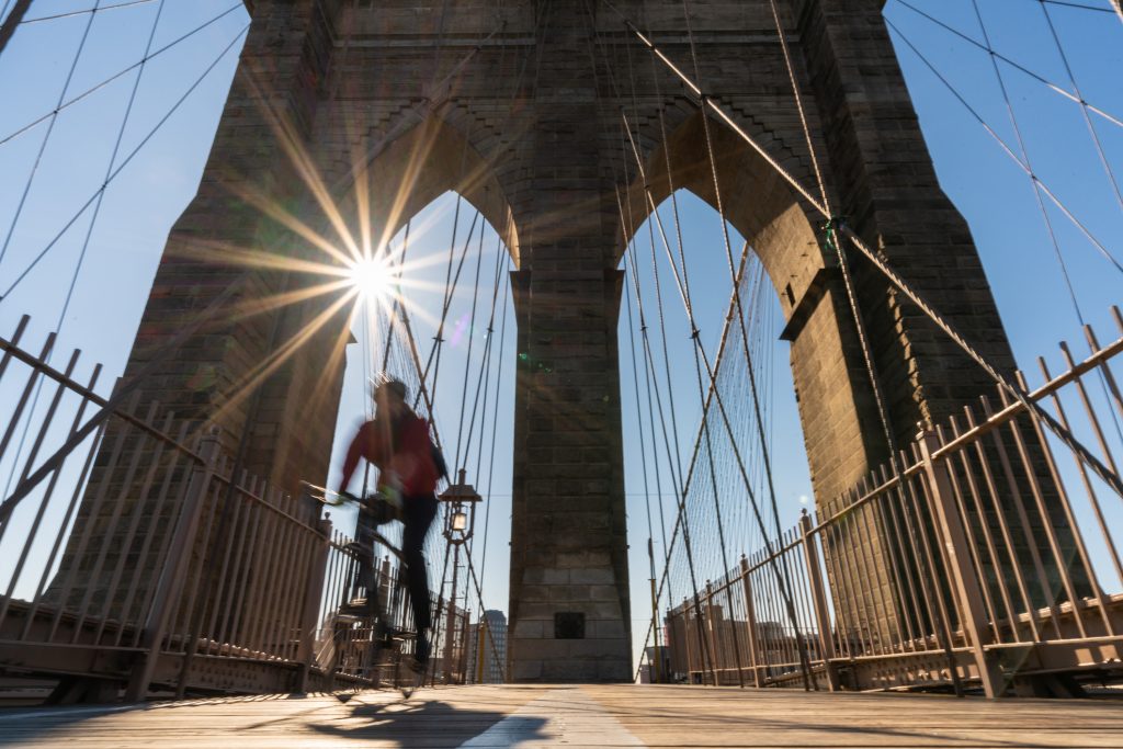 Scene of stop motion bicycle with Brooklyn bridge when sunrise, USA downtown skyline, Architecture and building with tourist concept