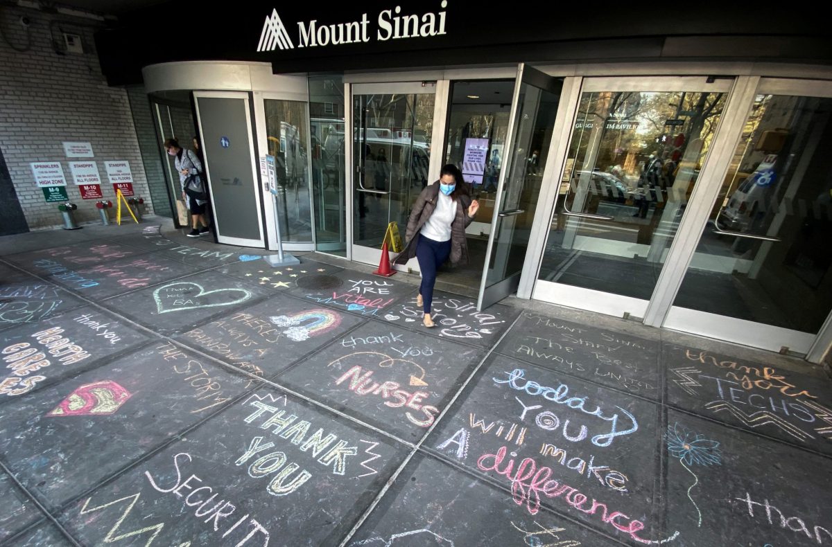 Woman exits Mount Sinai Hospital past messages of thanks to healthcare workers written on sidewalk in New York