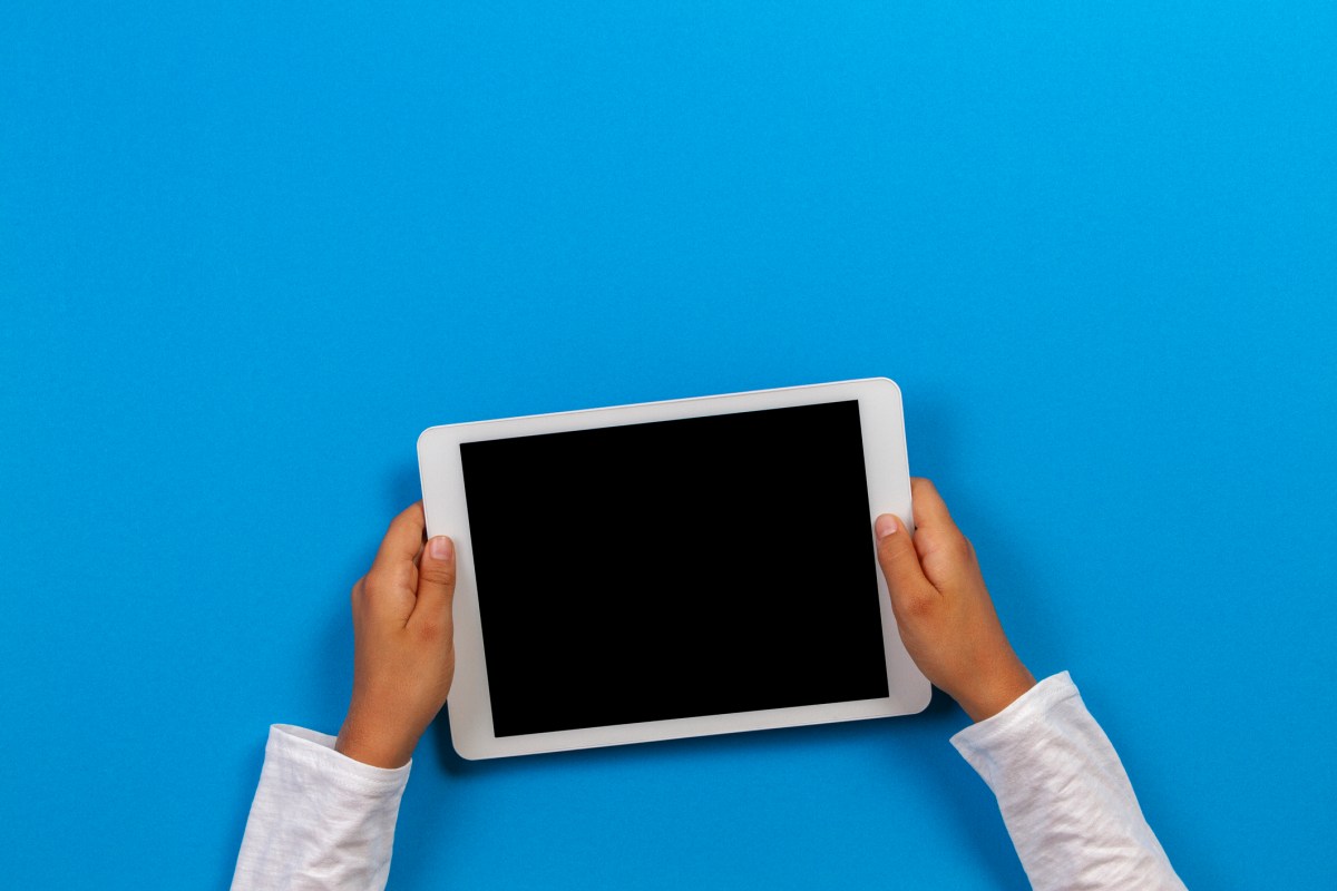Kid hand holding white tablet computer on light blue background