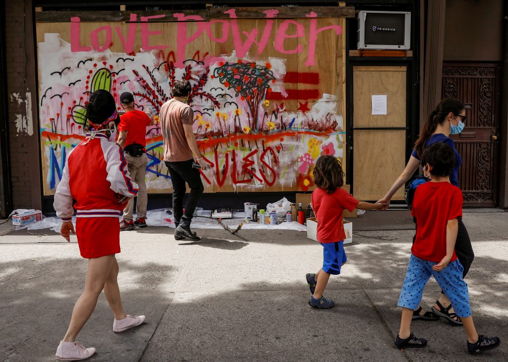 Artists paint a mural on a boarded-up storefront as part of neighborhood project in the Bowery neighborhood of New York