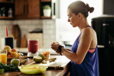 Athletic woman slicing fruit while preparing smoothie in the kitchen.