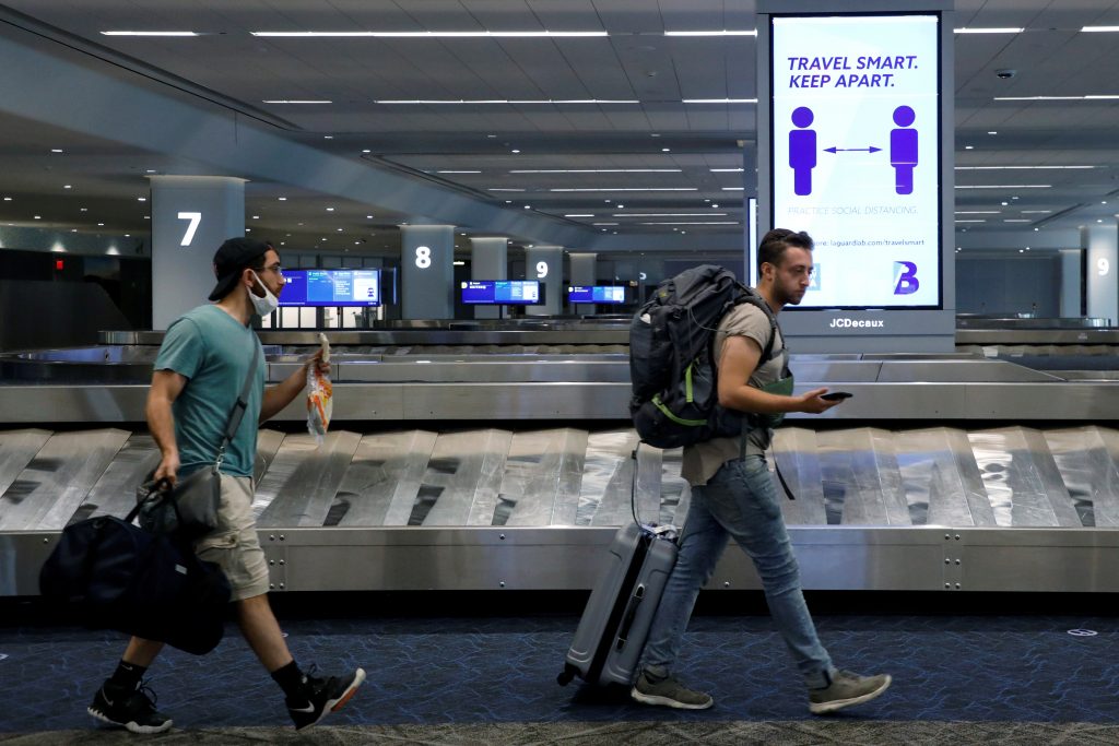 FILE PHOTO: Travelers pass a sign alerting them to distance at LaGuardia Airport, during the outbreak of the coronavirus disease (COVID-19), in New York