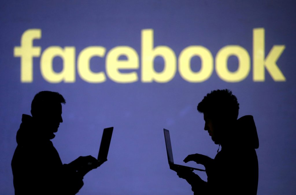 FILE PHOTO: Silhouettes of laptop users are seen next to a screen projection of a Facebook logo