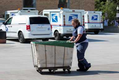 A United States Postal Service (USPS) worker pushes a mail bin outside a post office in Royal Oak