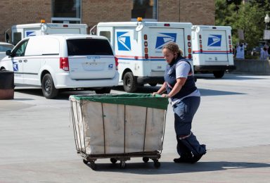 A United States Postal Service (USPS) worker pushes a mail bin outside a post office in Royal Oak