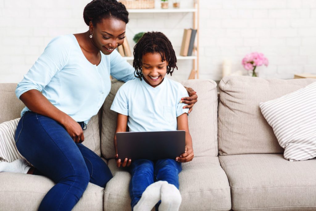 Afro mom and daughter using laptop on sofa
