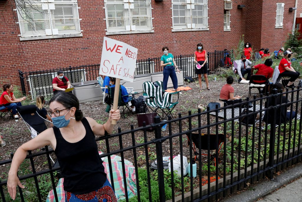 A parent holds a sign to protest the opening of schools, as teachers work outside their school building for safety reasons in Brooklyn, New York