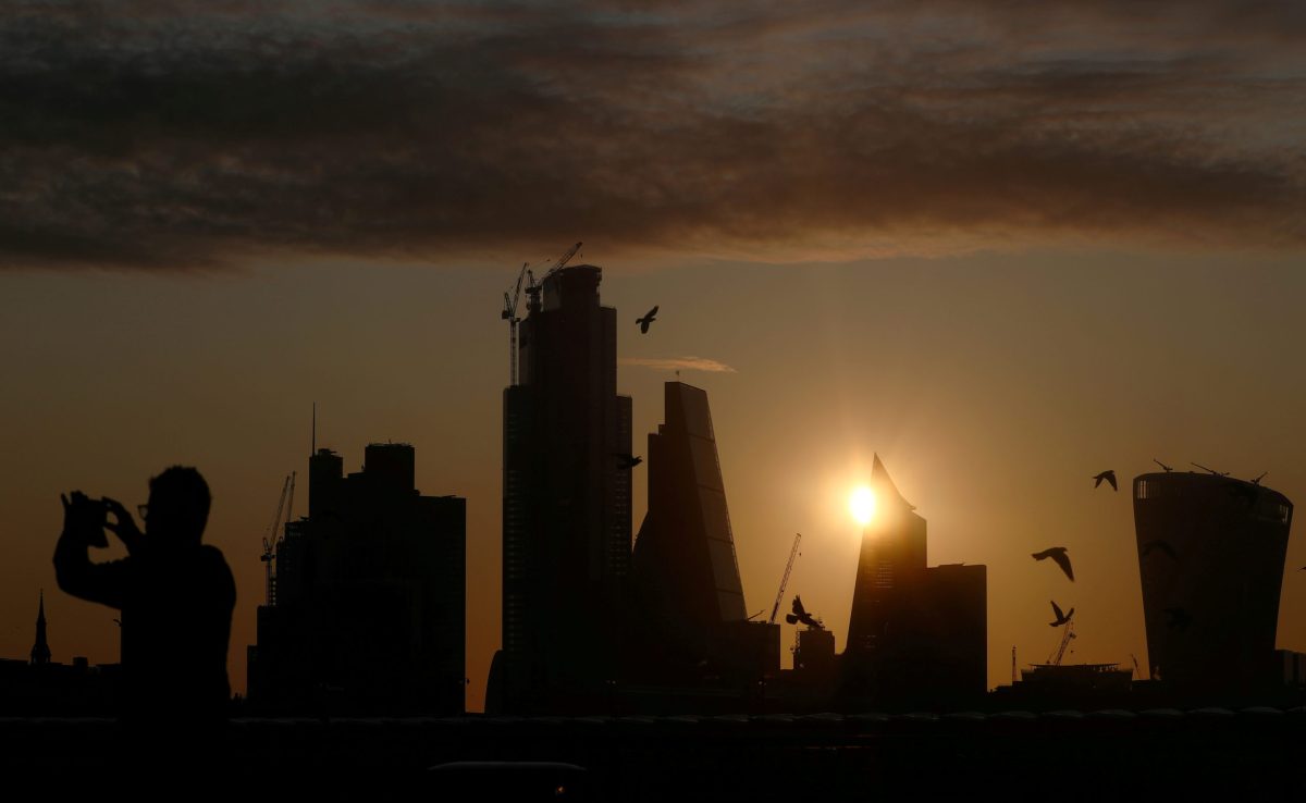 FILE PHOTO: A man takes a photograph of the skyline as the sun rises behind the city of London financial district in London