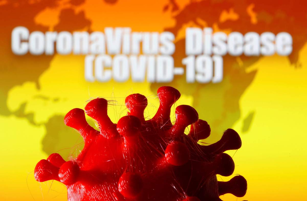 A 3D-printed coronavirus model is seen in front of a world map and the words “CoronaVirus Disease (Covid-19)” on display in this illustration