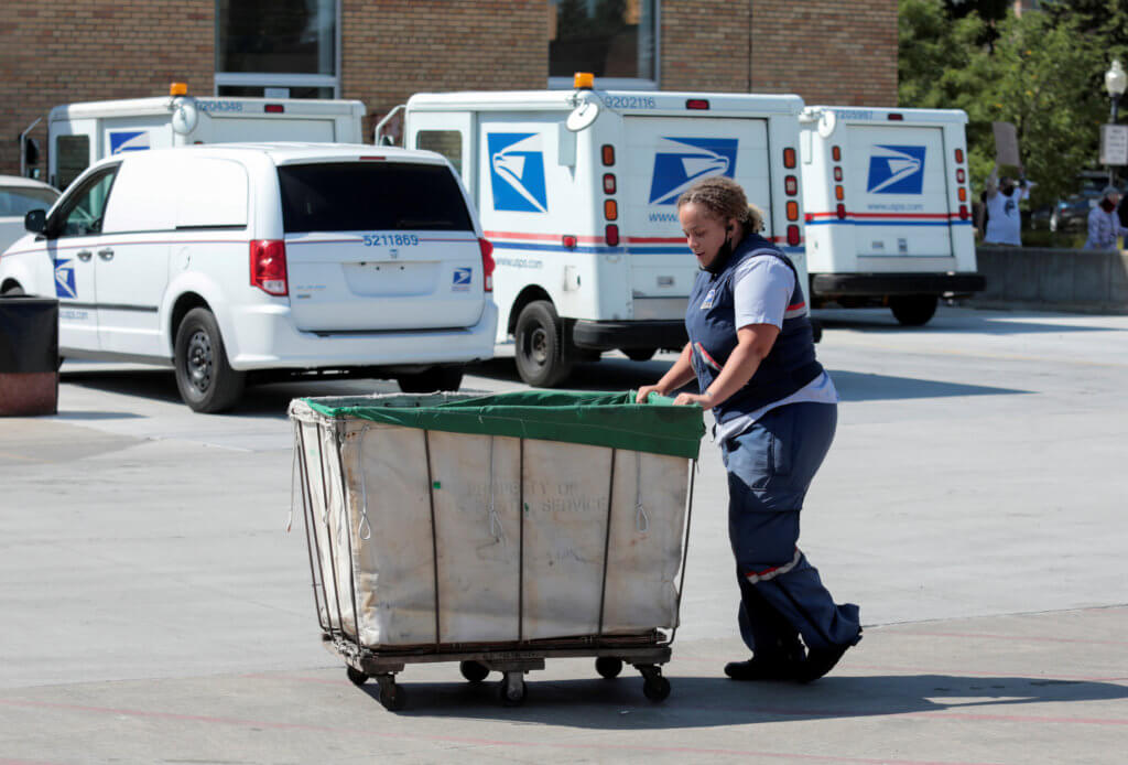 FILE PHOTO: A United States Postal Service (USPS) worker pushes a mail bin outside a post office in Royal Oak