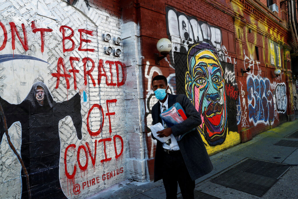 FILE PHOTO: A man wearing a protective face mask as he walks by murals as the spread of coronavirus disease (COVID-19) continues along Houston Street in New York City
