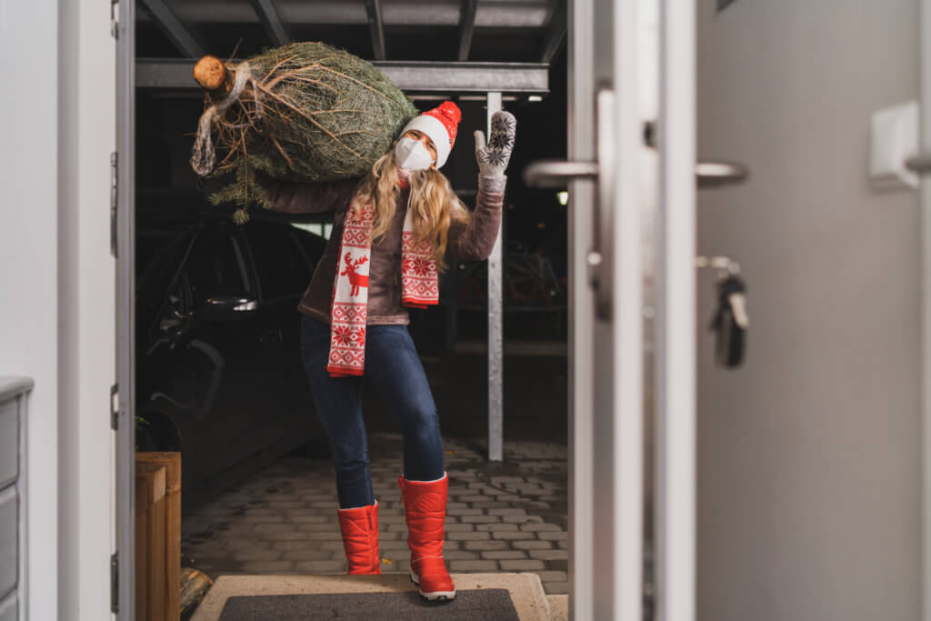 happy woman with mask delivering christmas tree at open door of house