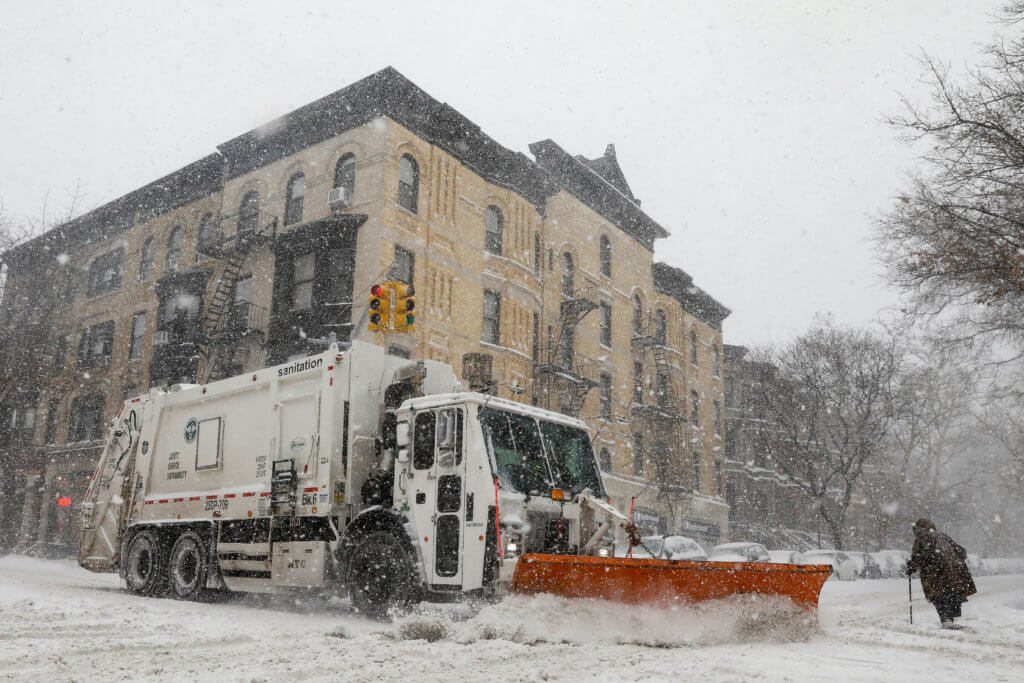 A garbage truck with a plow clears the street during a snowstorm in the Brooklyn borough of New York