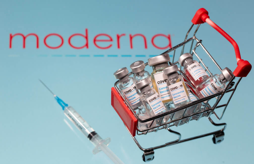 FILE PHOTO: A small shopping basket filled with vials labelled “COVID-19 – Coronavirus Vaccine” and a medical syringe are placed on a Moderna logo