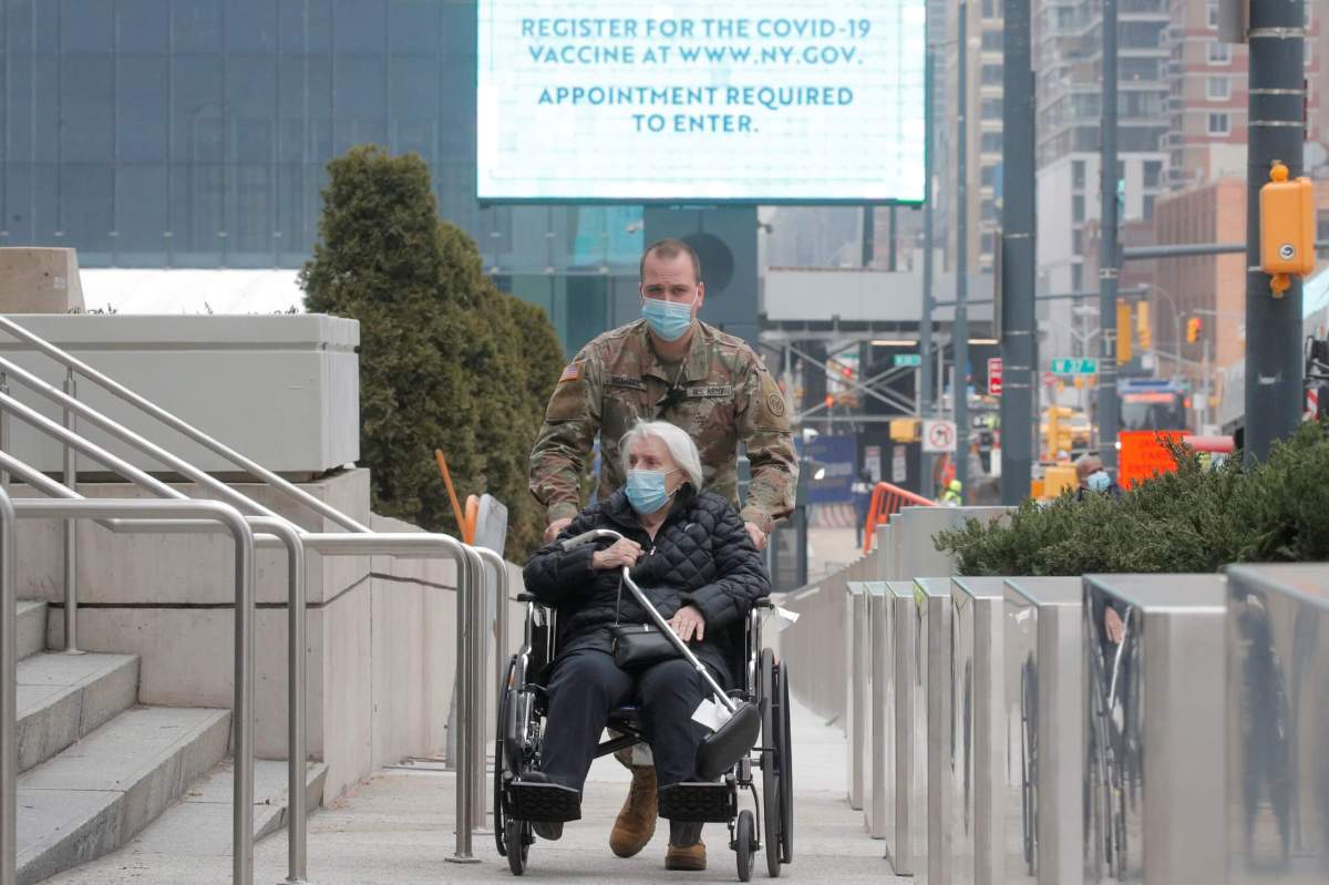 A soldier assists an elderly woman as she arrives to receive a dose of COVID-19 vaccine at the New York State vaccination site at the Jacob K. Javits Convention Center, in New York