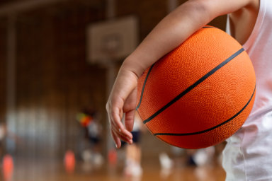 Schoolboy with basketball standing in basketball court