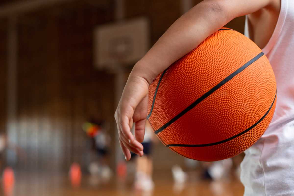 Schoolboy with basketball standing in basketball court