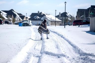 A man walks to his friend’s home in a neighbourhood without electricity as snow covers the BlackHawk neighborhood in Pflugerville