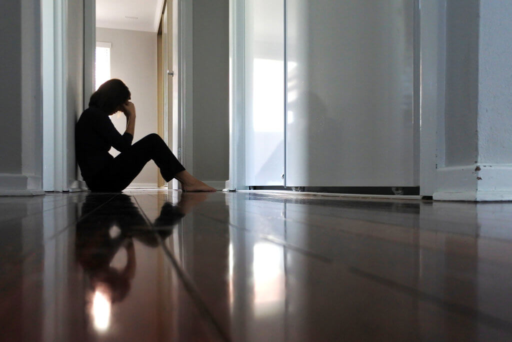 Woman sitting on dark home corridor floor.