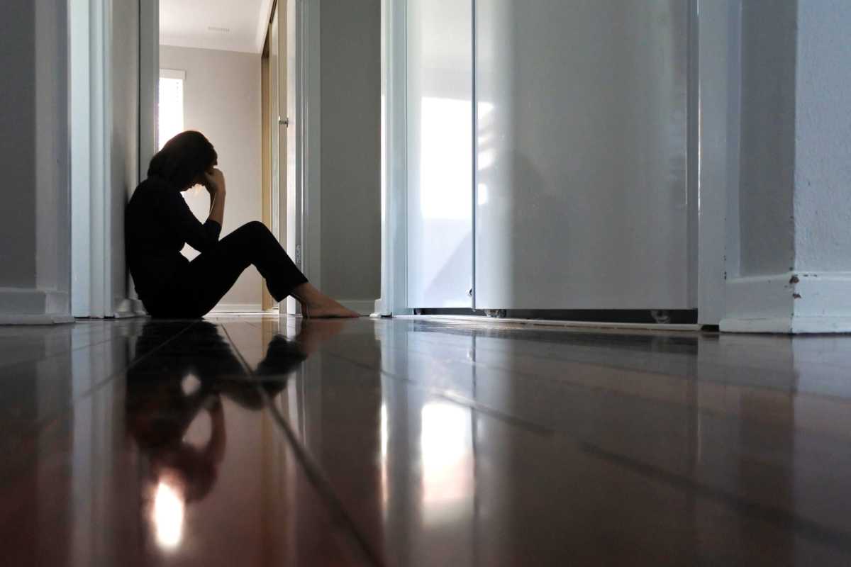 Woman sitting on dark home corridor floor.