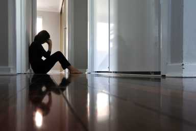 Woman sitting on dark home corridor floor.