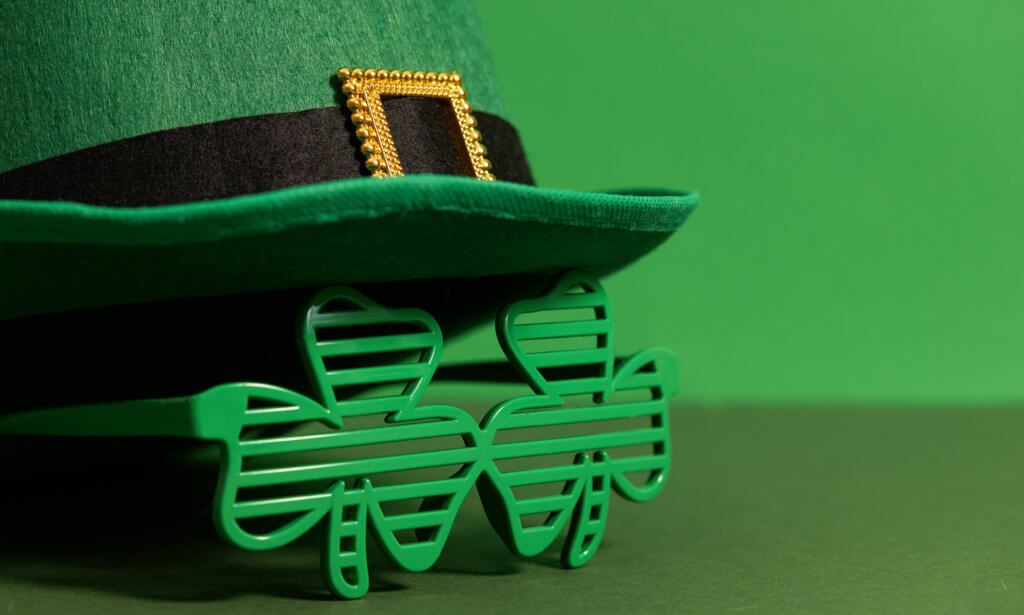Happy St Patricks Day. Lepricon hat with glasses in the shape of a three leaf clover on a green background. Holiday attributes