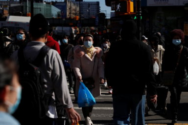 People wearing protective face masks walk down Main Street in the Flushing area of the Queens borough in New York City
