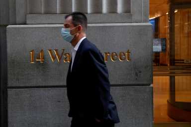 FILE PHOTO: A man wearing a protective face mask walks by 14 Wall Street, as the global outbreak of the coronavirus disease (COVID-19) continues, in the financial district of New York