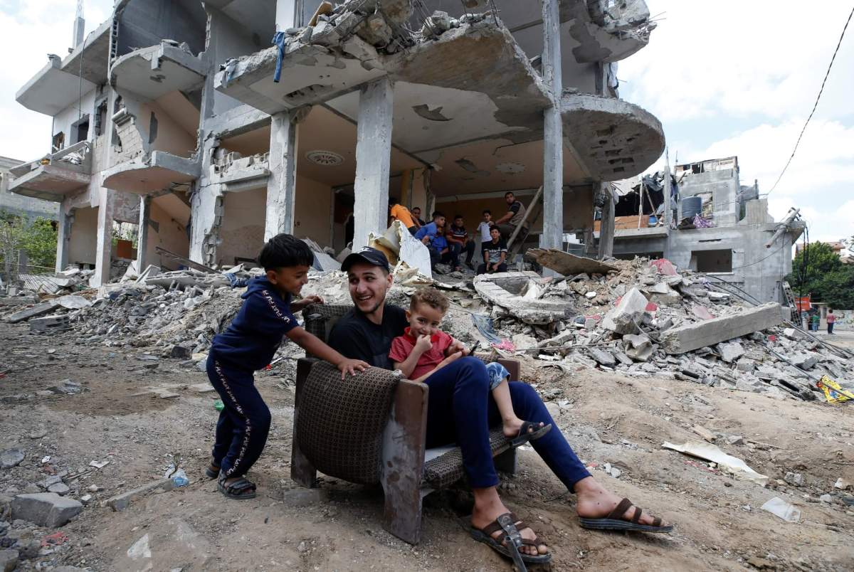 Palestinians sit on chair in front of a building which was damaged in Israeli air strikes