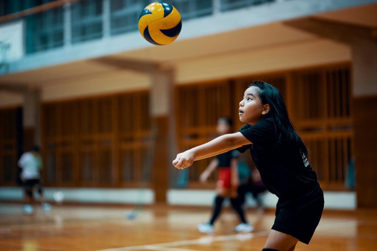 Young girl playing volleyball at a team practice in a school gym