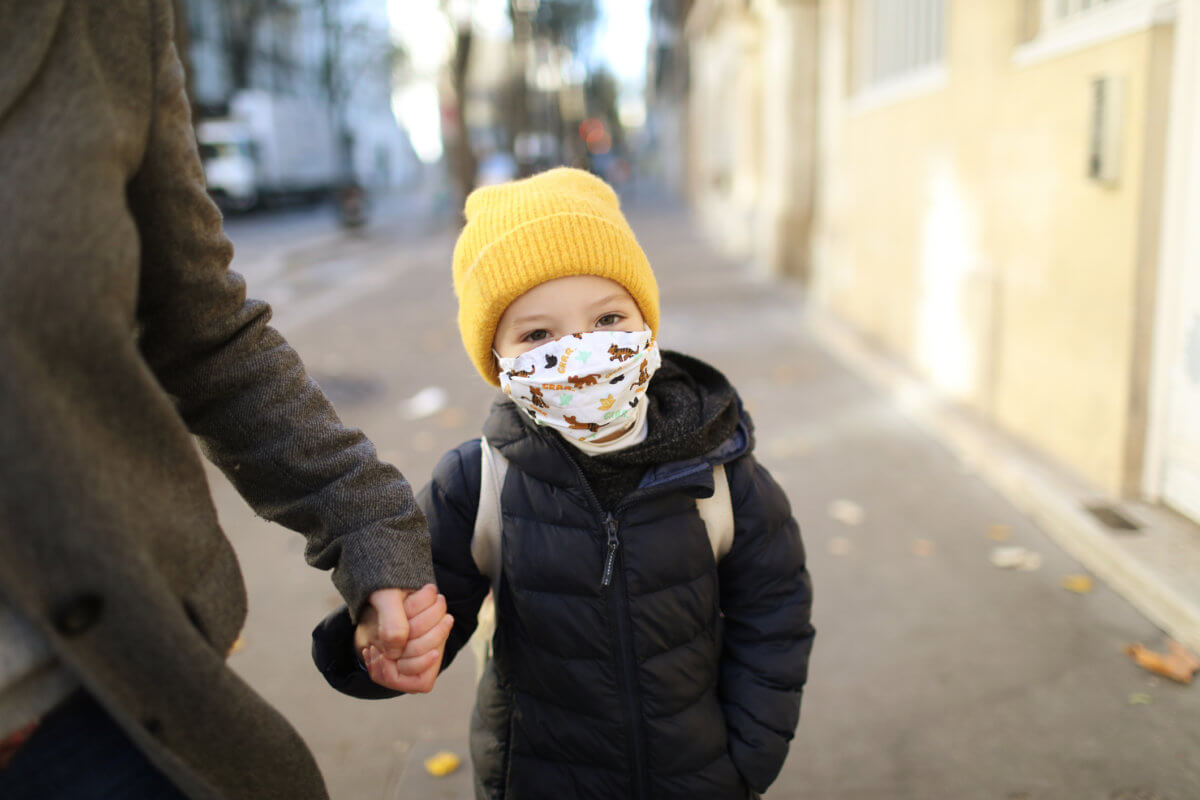 A little girl wearing a protective face mask, holding the hand of her mother in the street before to go to school