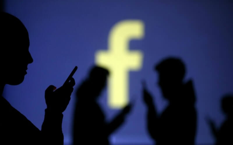 Silhouettes of mobile users are seen next to a screen projection of Facebook logo in this picture illustration