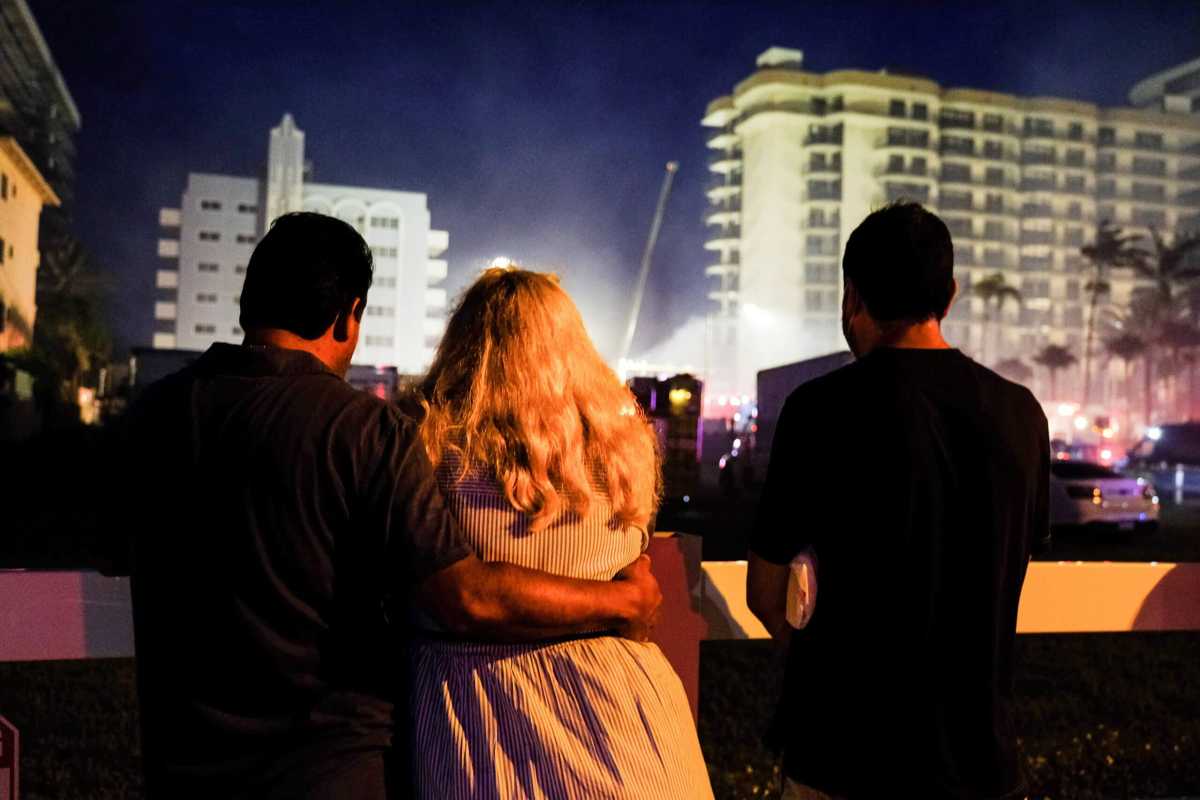 FILE PHOTO: People stand near the partially collapsed residential building in Surfside, as the emergency crews continue search and rescue operations for survivors