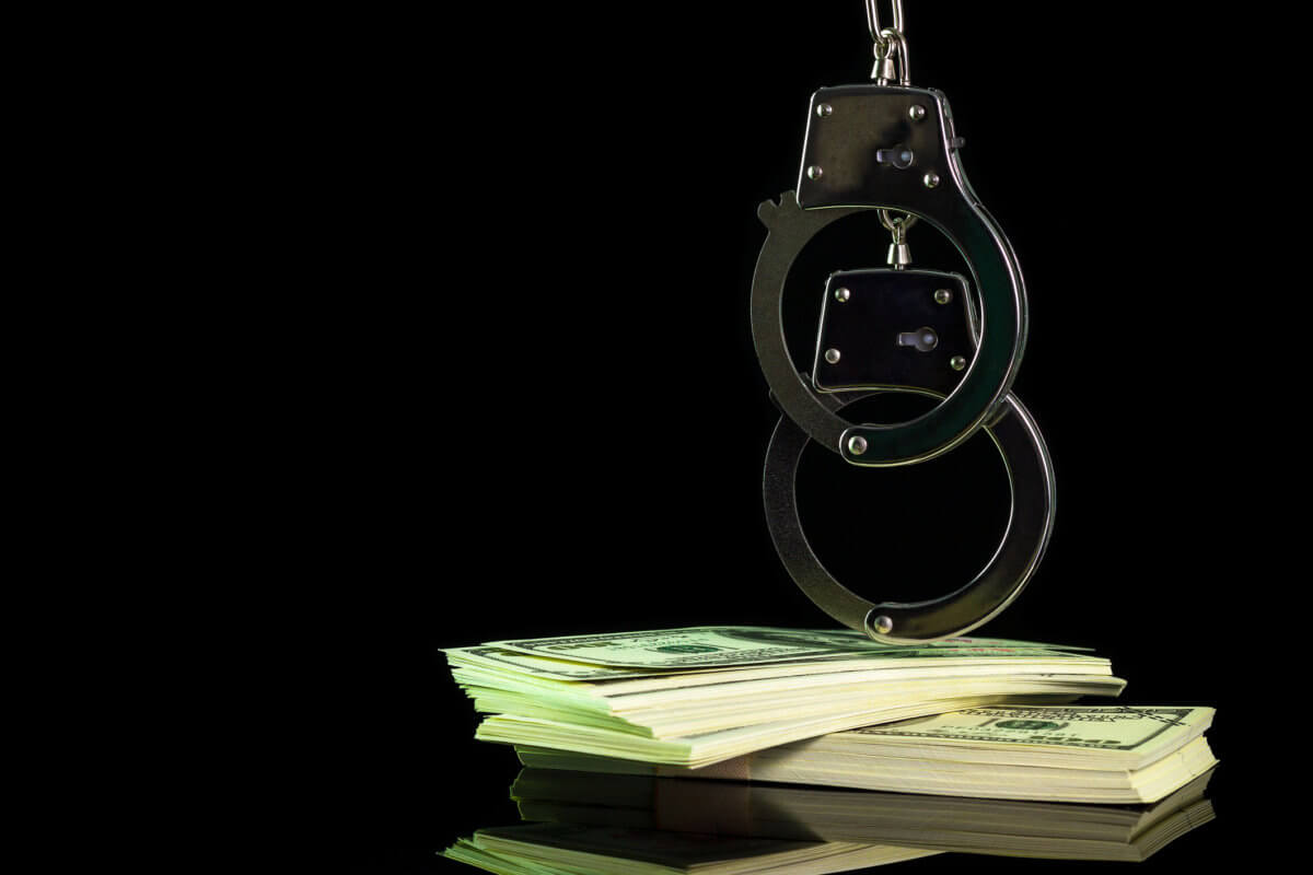 Handcuffs were hung on a dollar banknote in darkness background.