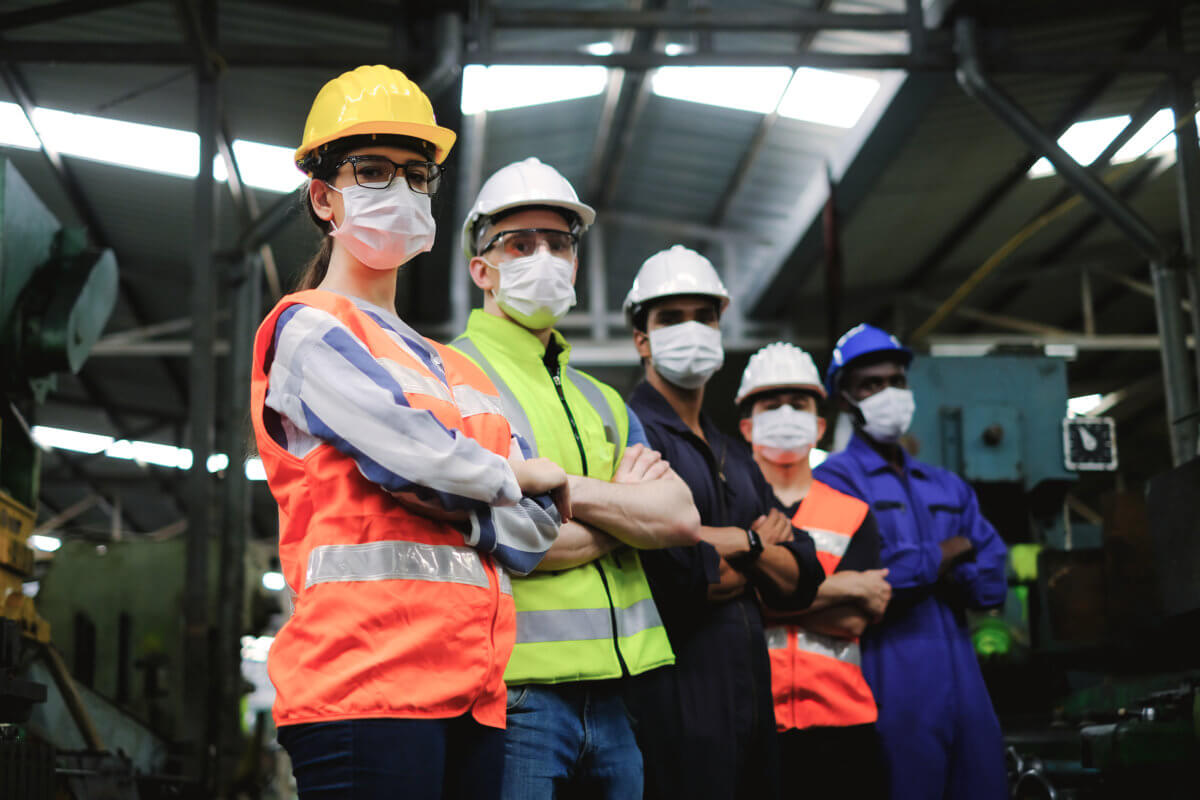 woman engineer wearing  hygiene face mask and hardhat with workers in factory